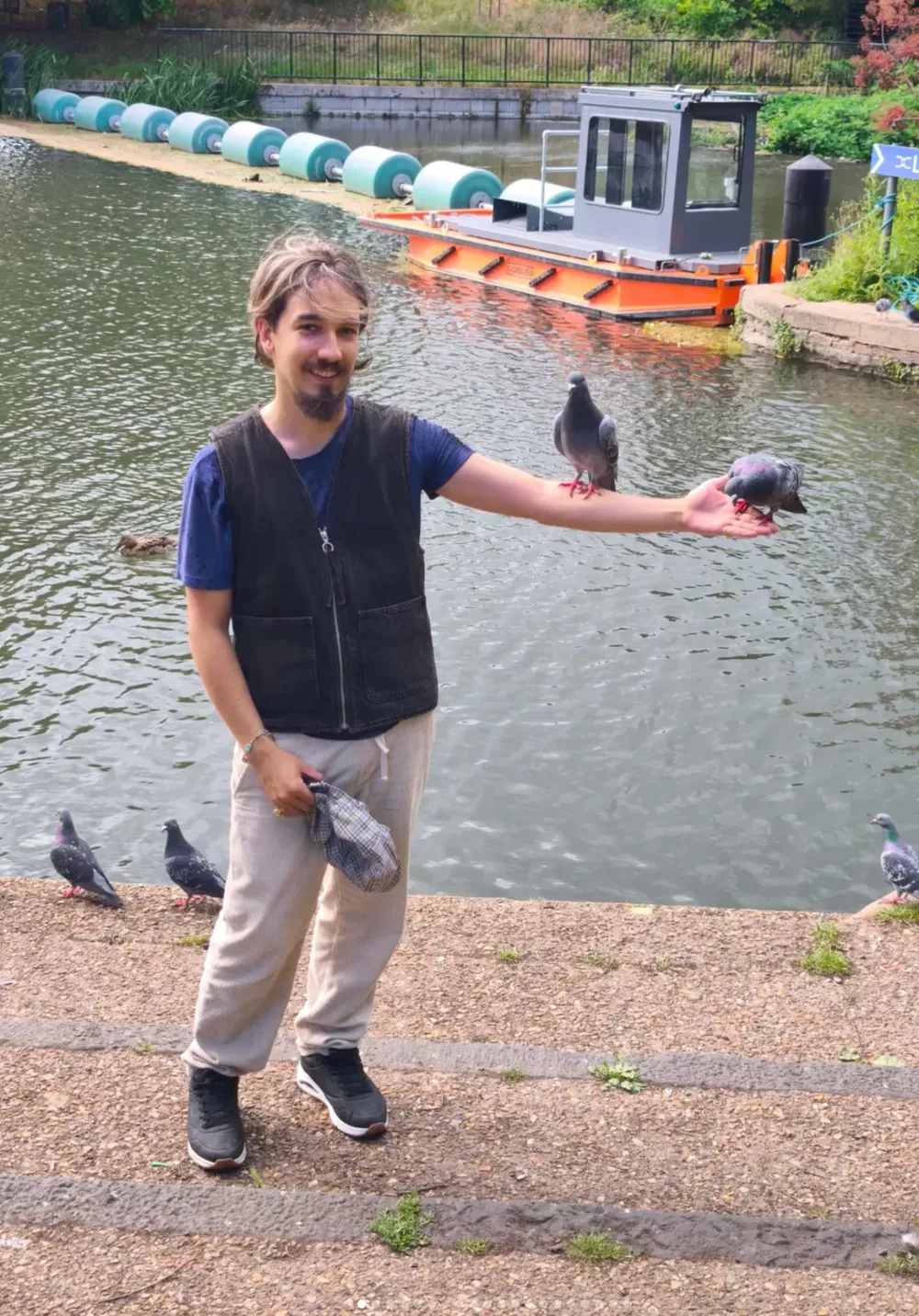 Efe smiling beside a canal with pigeons perched on his arm.